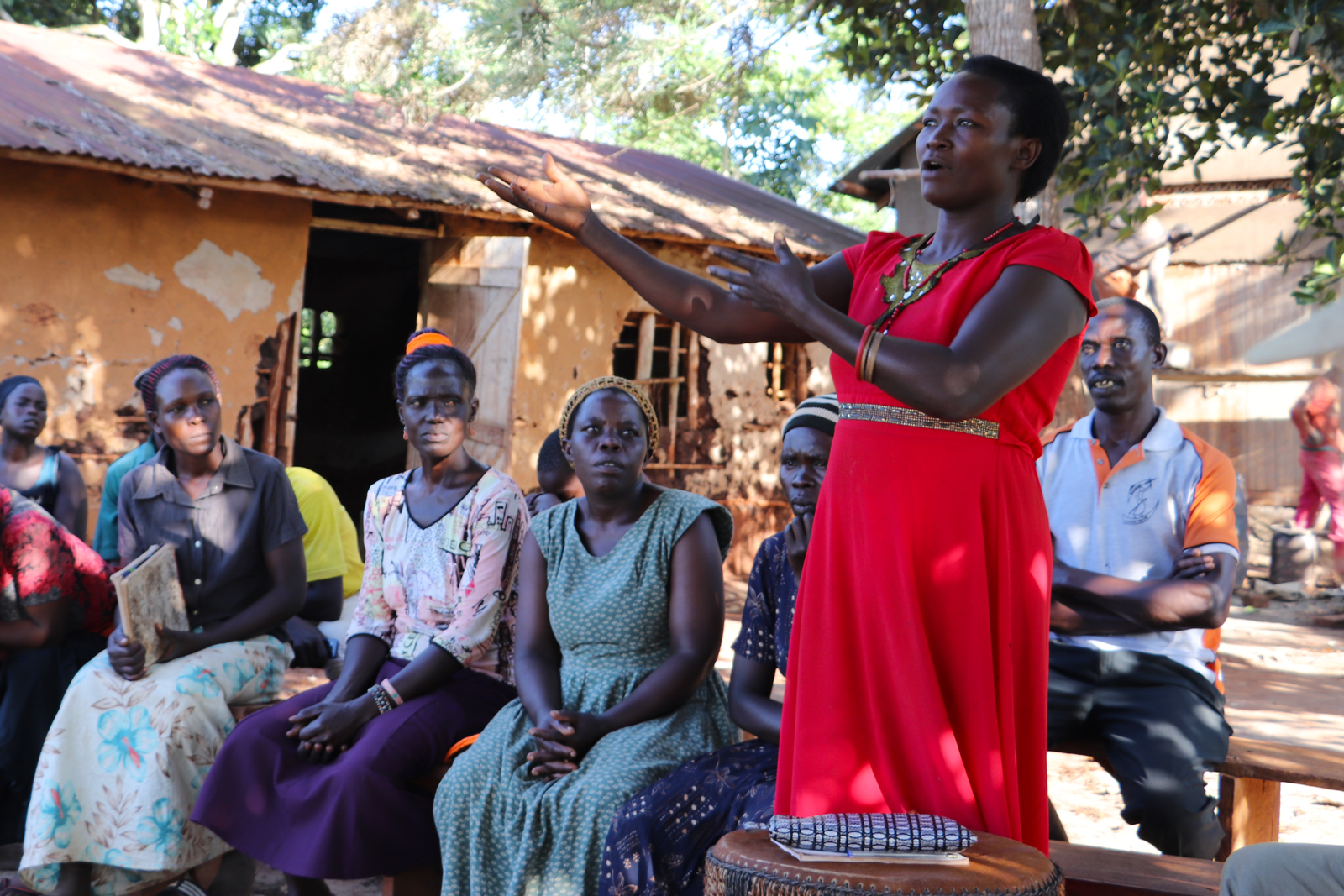 At an outdoor meeting of farmers in Uganda, a woman stands and speaks to the group